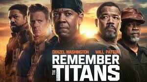 *"Denzel Washington as Coach Boone stands arms crossed in a football jacket, leading his racially diverse team in blue and gold uniforms. The title 'Remember the Titans' appears in bold white letters against a stormy sky."