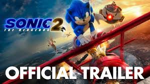 Sonic the Hedgehog, a blue anthropomorphic hedgehog with red sneakers, grins mid-run as his golden quills glow with electricity. Beside him, Miles "Tails" Prower, a small orange fox with two spinning tails, flies eagerly. Knuckles the Echidna, a muscular red warrior with spiked gloves, stands poised for battle in the background. Villain Dr. Robotnik, a wild-eyed man in a black coat, hovers in a high-tech mech, grinning maniacally. The group is set against a vibrant landscape of lush green hills and loop-de-looping roads, capturing the film's high-energy adventure.