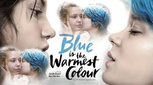 Adèle (Adèle Exarchopoulos), a young woman with tousled brown hair and intense eyes, gazes longingly at Emma (Léa Seydoux), a confident woman with striking blue-tipped hair, as they sit close together in a crowded artist's studio. Sunlight streams through the windows, casting warm golden tones across their faces, while Emma's vibrant blue highlights mirror the cerulean paint smudged on her fingertips. Their body language conveys deep intimacy - Adèle's slightly parted lips and Emma's protective hand resting near her knee suggest an unspoken emotional connection.