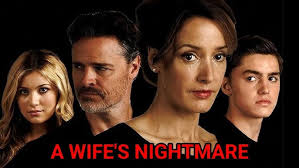 A tense thriller movie poster showing a distressed woman (Vanessa) standing in a dimly lit hallway, clutching a phone while glancing over her shoulder. Behind her, a shadowy figure (Claire) lurks near a doorway, creating an atmosphere of suspense. The title "A Wife’s Nightmare" appears in bold red letters, hinting at danger and betrayal.