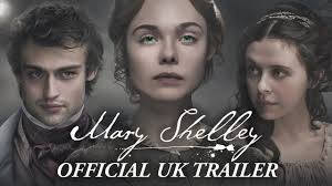 "Elle Fanning as young Mary Shelley, her pale face framed by dark Romantic-era curls, gazes solemnly past the viewer. A stormy blue backdrop with faint scripted handwriting evokes the creation of Frankenstein. Gold text reads 'Mary Shelley' with 'The author behind the monster' below."