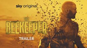 "Jason Statham as a retired operative in beekeeping gear, holding a smoker, standing in front of a fiery explosion. The dark, intense backdrop suggests an action-packed revenge thriller."