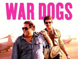 "Two young arms dealers, played by Jonah Hill and Miles Teller, stand in a desert wearing casual clothes, surrounded by military vehicles and crates of weapons. The scene captures the darkly comedic tone of their risky business ventures during the Iraq War."