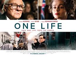 "Young Nicholas Winton (Johnny Flynn) in a 1930s suit urgently speaks with officials at a crowded Prague train station. Jewish children with tags around their necks board a Kindertransport train to safety as Nazi threats loom."