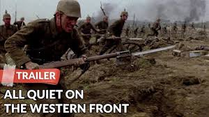 "Paul Bäumer (Felix Kammerer), a mud-covered German soldier with hollow eyes, crouches in a waterlogged trench amid barbed wire and corpses, his rifle trembling in his hands."