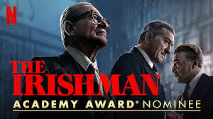 "A still from The Irishman showing Frank Sheeran (Robert De Niro) and Jimmy Hoffa (Al Pacino) in a heated conversation at a restaurant, with warm lighting and tense body language."